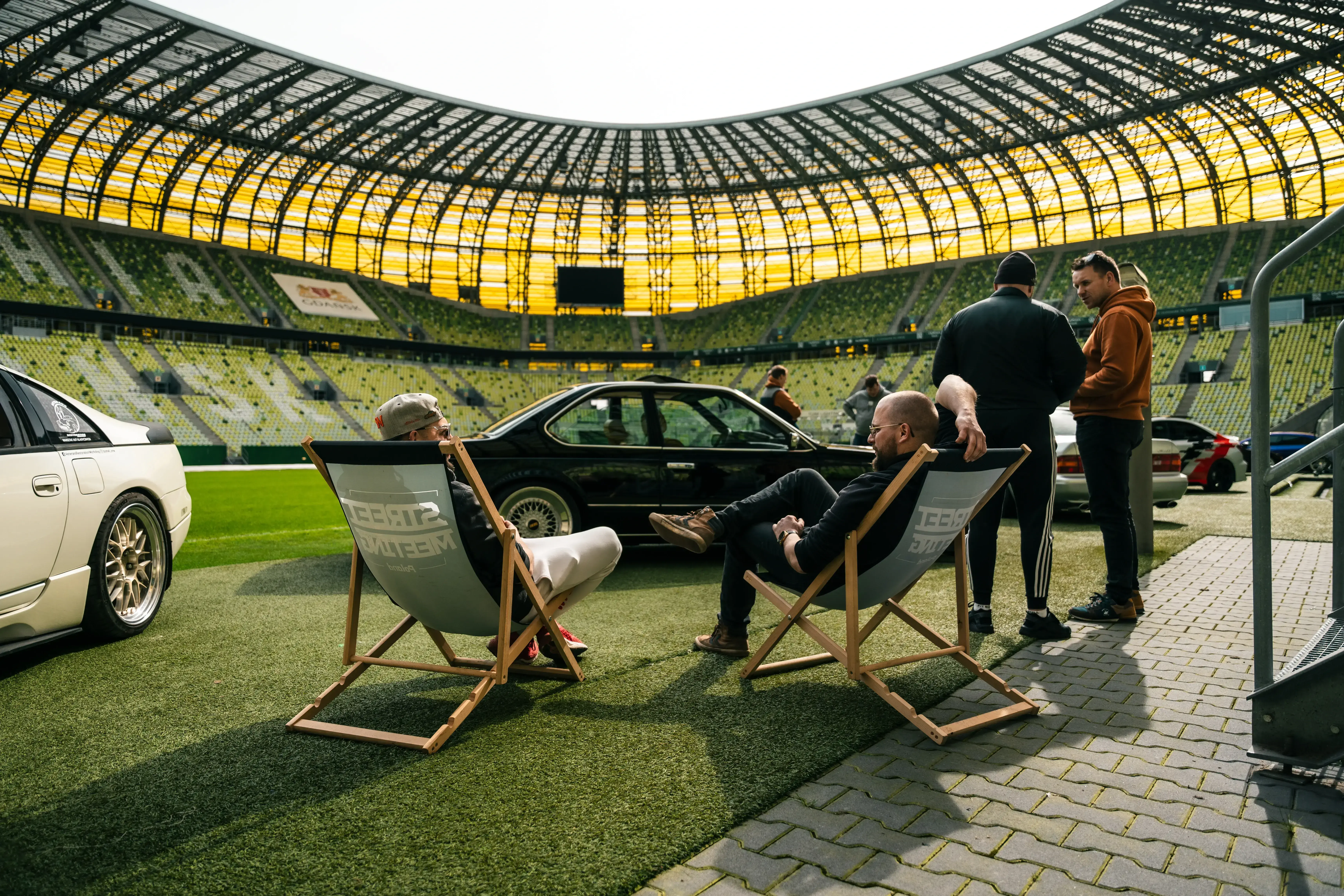 Samochody na murawie Polsat Plus Arena, Gdańsk, a na przodzie składane krzesełka z napisem street meeting